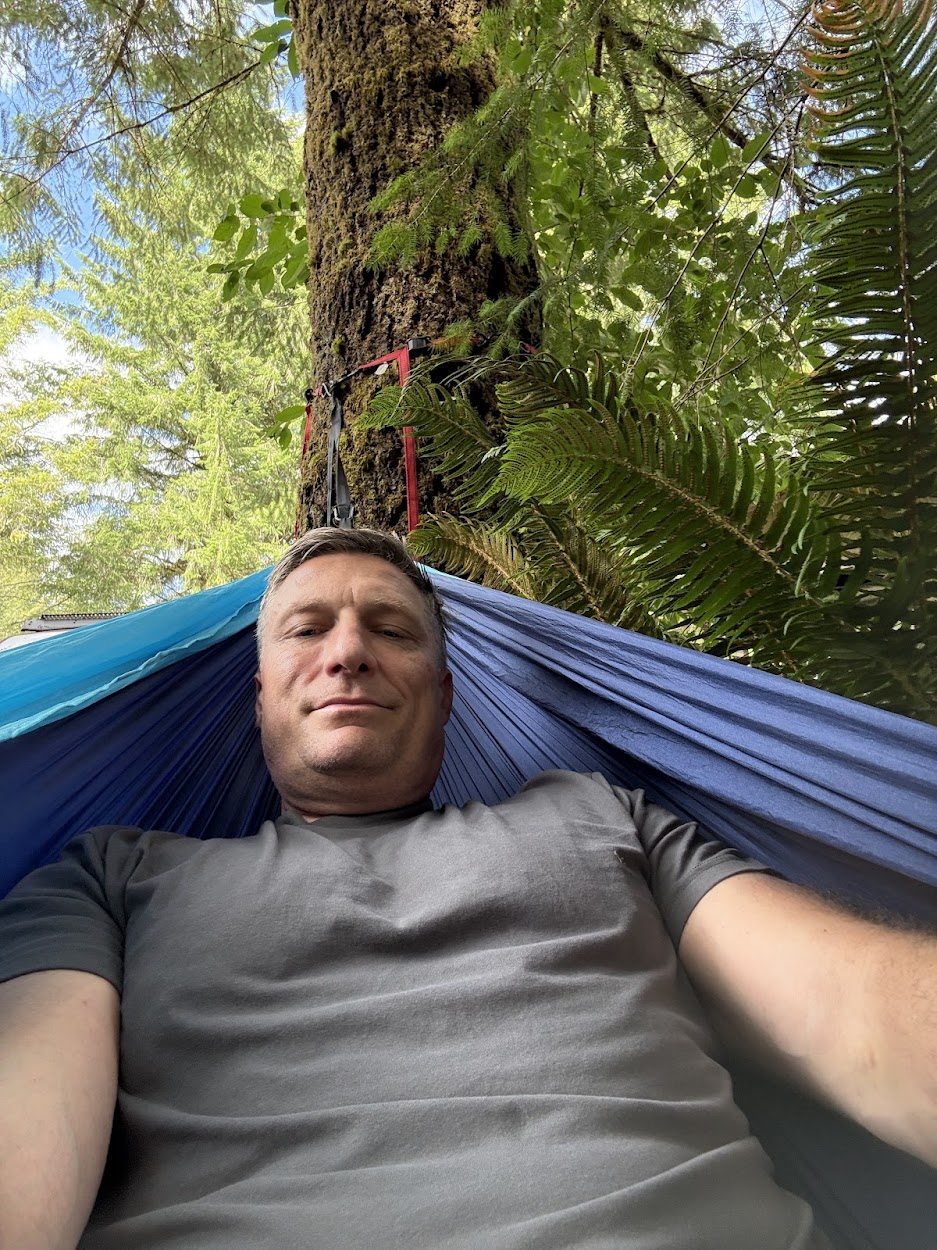 Jason Fox relaxing in a hammock among the trees at Lake Tyee.